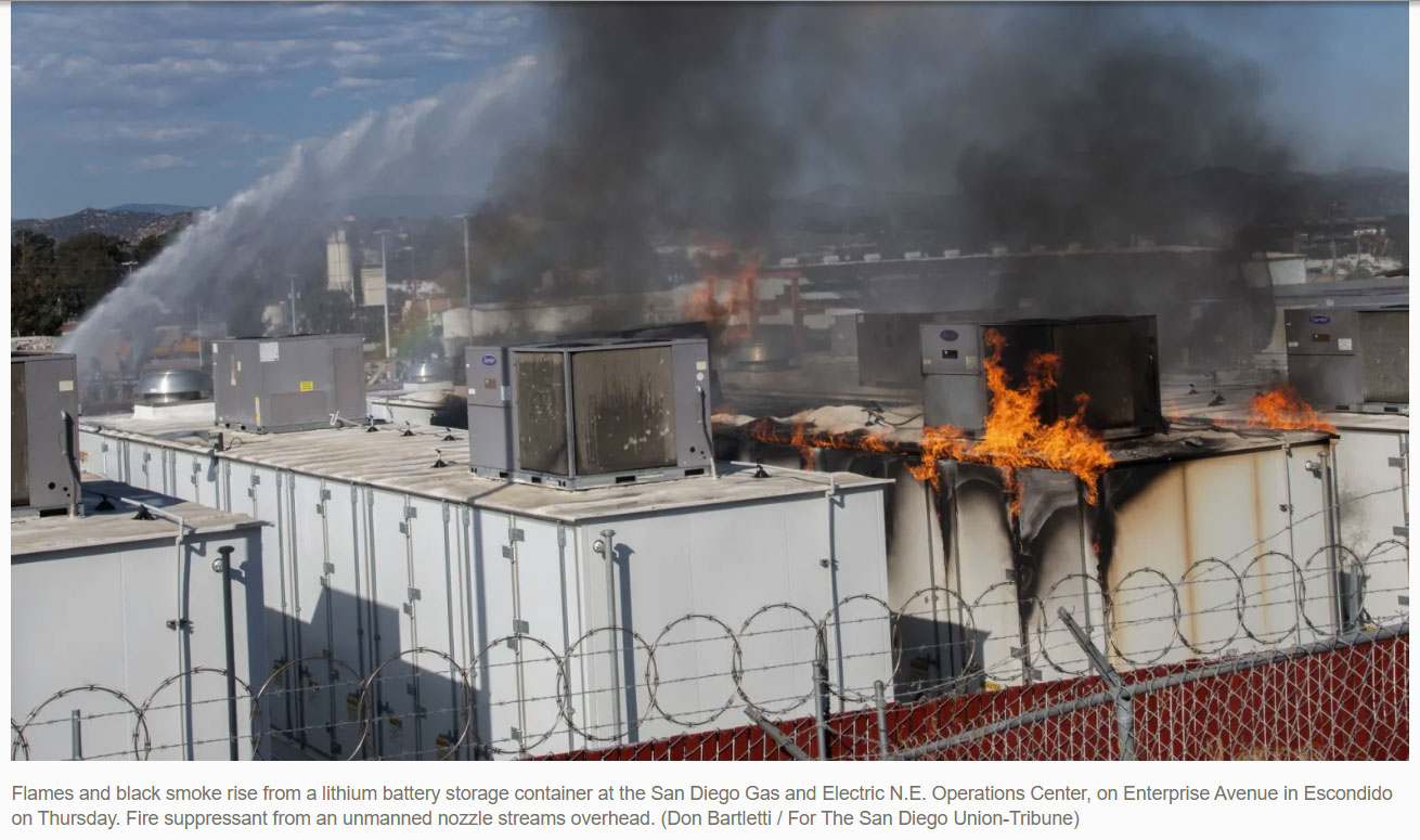 Flames and black smoke rise from a lithium battery storage container at the San Diego Gas and Electric N.E. Operations Center, on Enterprise Avenue in Escondido on Thursday. Fire suppressant from an unmanned nozzle streams overhead. (Don Bartletti / For The San Diego Union-Tribune)